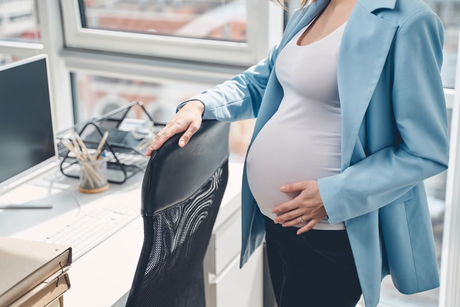 Young pregnant woman standing by office chair