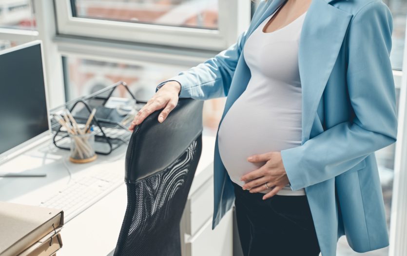 Young pregnant woman standing by office chair